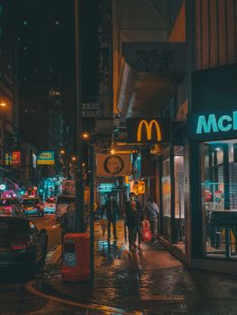 雨夜，一位匿名人士走在市中心灯火通明的商店和餐厅附近的街道上