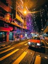 夜晚，一辆复古出租车停在现代城市明亮的建筑旁，在人行横道前等候