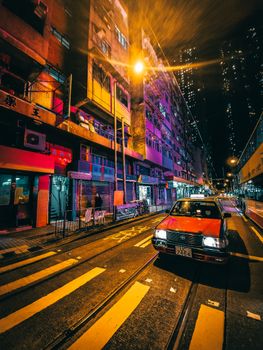 夜晚，一辆复古出租车停在现代城市明亮的建筑旁，在人行横道前等候