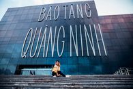 From below of young cheerful female in trendy outfit relaxing on stairs of modern building with glass walls and smiling
