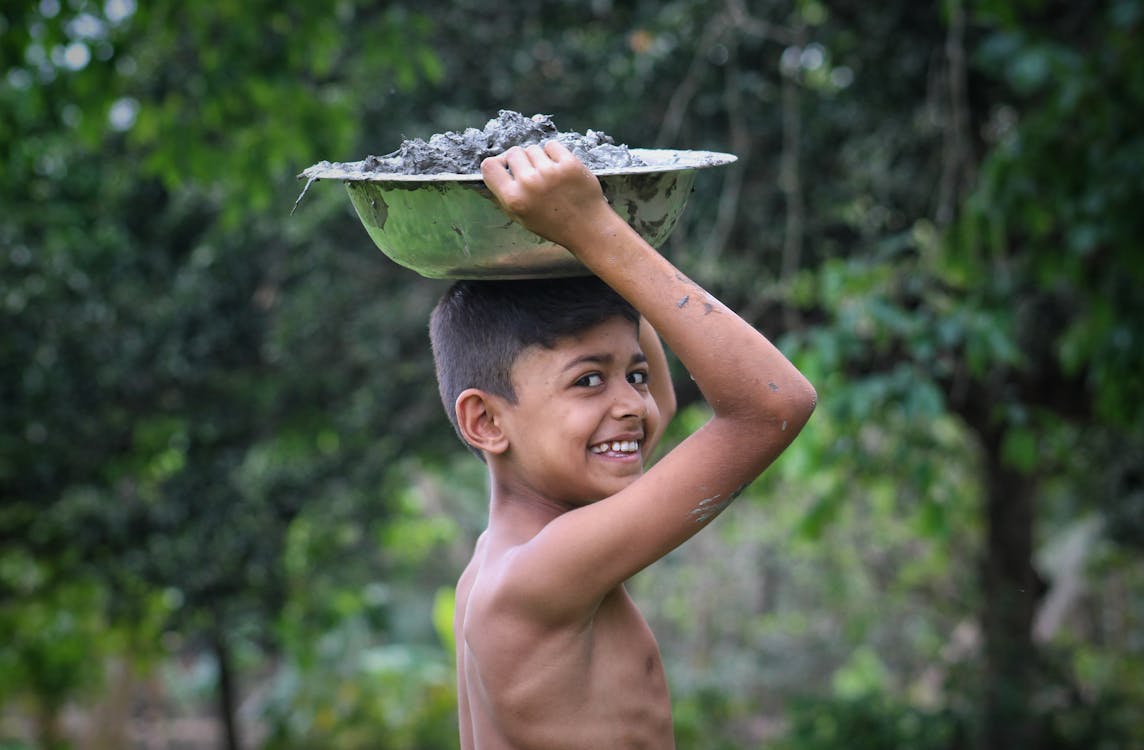 Happy Indian boy carrying metal bowl on head