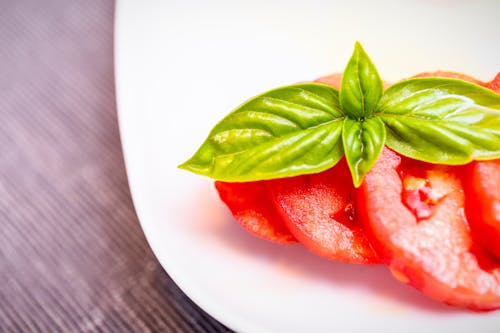 Sliced Tomato  and Basil Leaves on a White Ceramic Plate