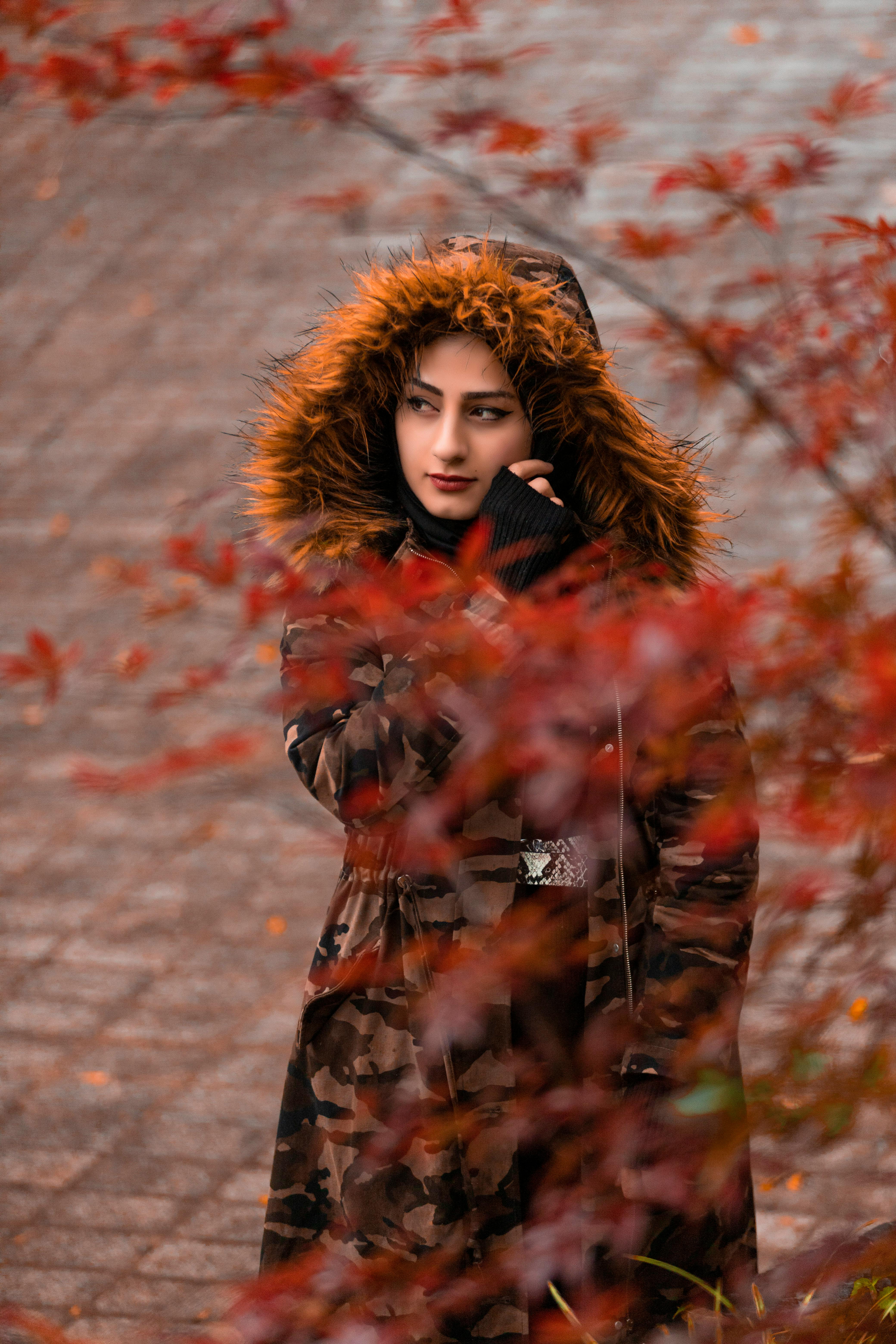 一位穿着温暖外套、戴着兜帽的宁静年轻女性，在秋日公园的小径上，目光移开，缓步前行