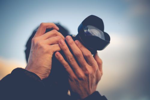 Free Hands holding a DSLR camera with a large lens, blurred background for effect. Stock Photo