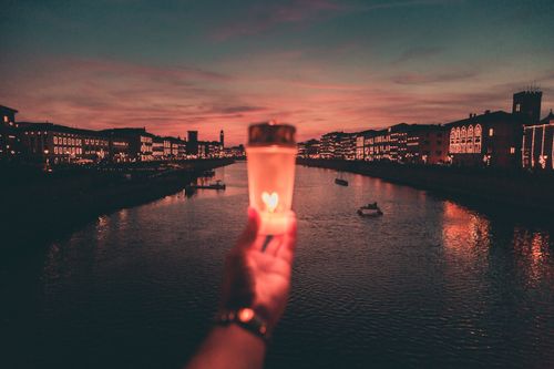 Free A serene scene of an illuminated candle held over the Arno River in Pisa at twilight, capturing the magical lights of the city. Stock Photo