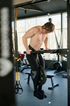A muscular man performing a weighted dip exercise at a modern gym.