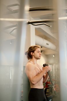Young male bodybuilder performing bicep curls in a modern gym, demonstrating strength and fitness.