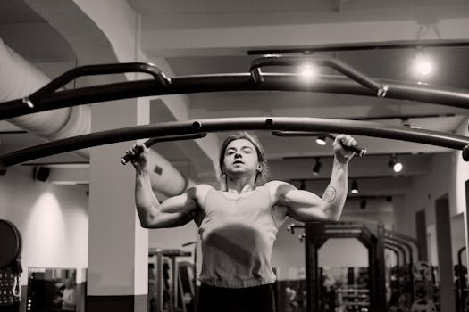 Grayscale image of a man doing pull-ups in a gym, showcasing strength and focus.