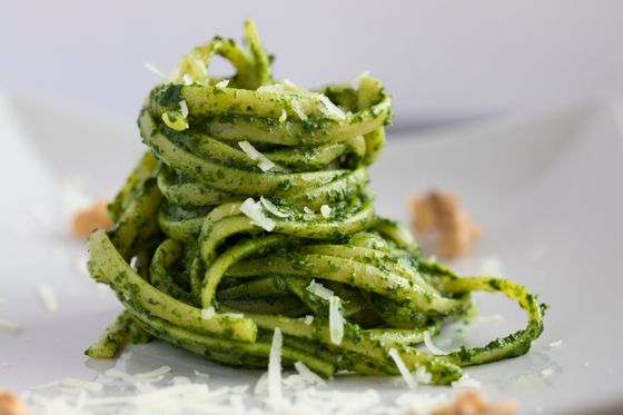 Tall nest of linguine coated in green basil pesto with parmesan shavings