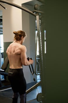 Back view of a muscular man working out with gym equipment, focusing on strength training.