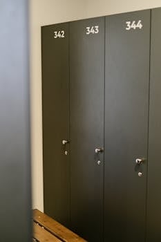 Contemporary gym locker room featuring dark lockers with numbers and wooden seating.