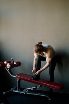 Muscular man preparing for workout, tying shoes in a modern gym environment.
