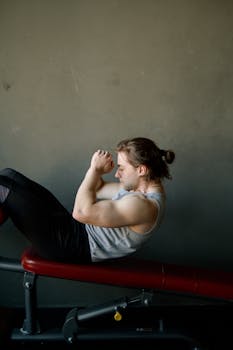 Man performing a workout on a bench in a gym, showcasing effort and strength.