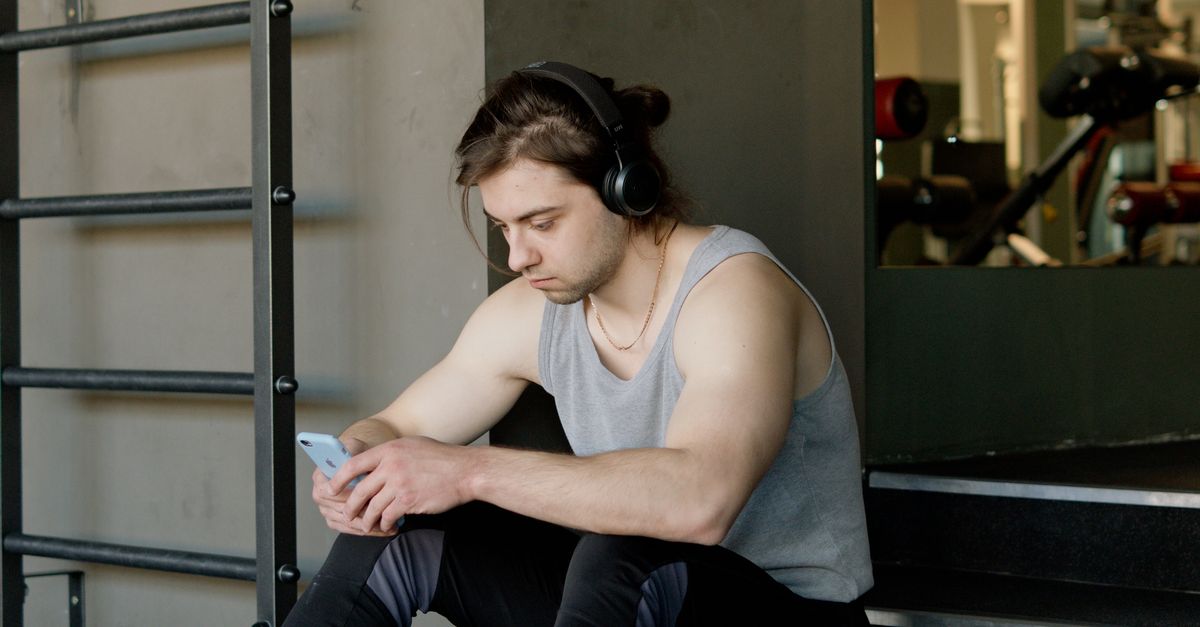 Young man in gym attire sitting on stairs with headphones and smartphone.