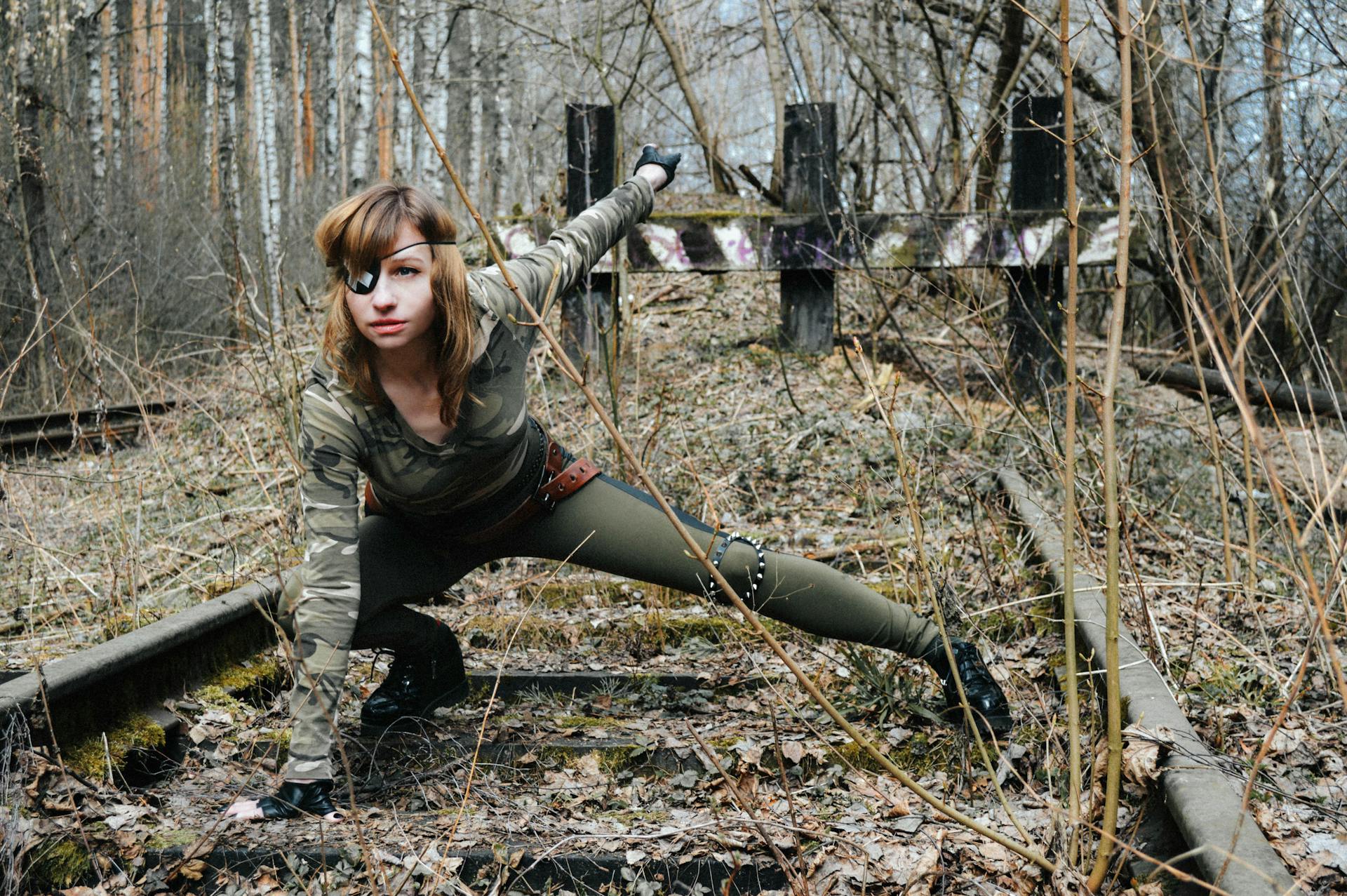 Confident young female soldier in camouflage and eye patch sitting on railway in autumnal woods