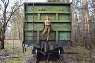 Slim woman wearing modern camouflage outfit with eye patch standing on aged green train in woods