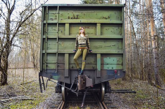 Slim woman wearing modern camouflage outfit with eye patch standing on aged green train in woods