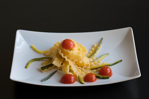Mafaldine pasta with chopped red tomatoes and green sprigs on white table on black background