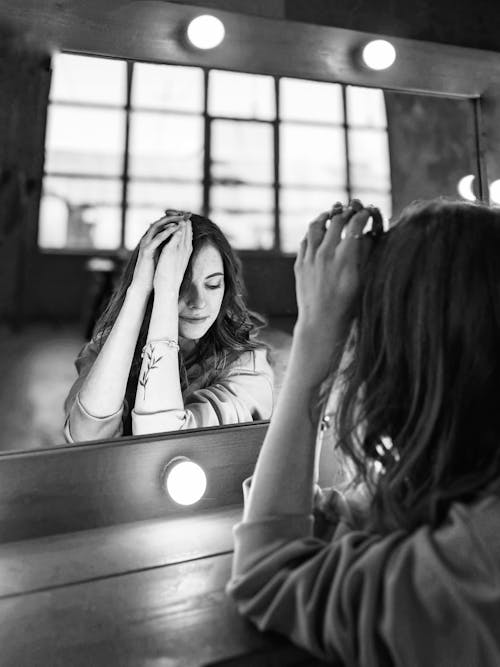 Grayscale Photo of Woman Sitting in Front of the Mirror