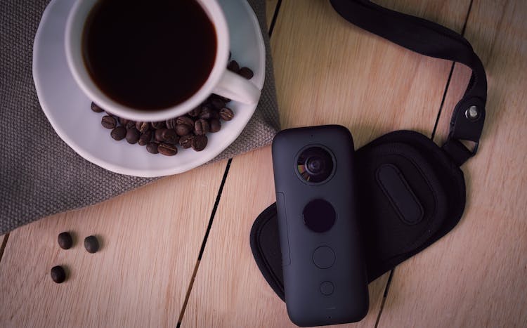 Cup Of Coffee With Beans On Table With Contemporary Small Video Camera