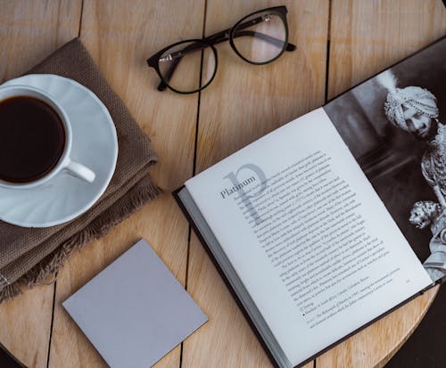 Free Opened book and sticky note placed on table with coffee cup and eyeglasses Stock Photo