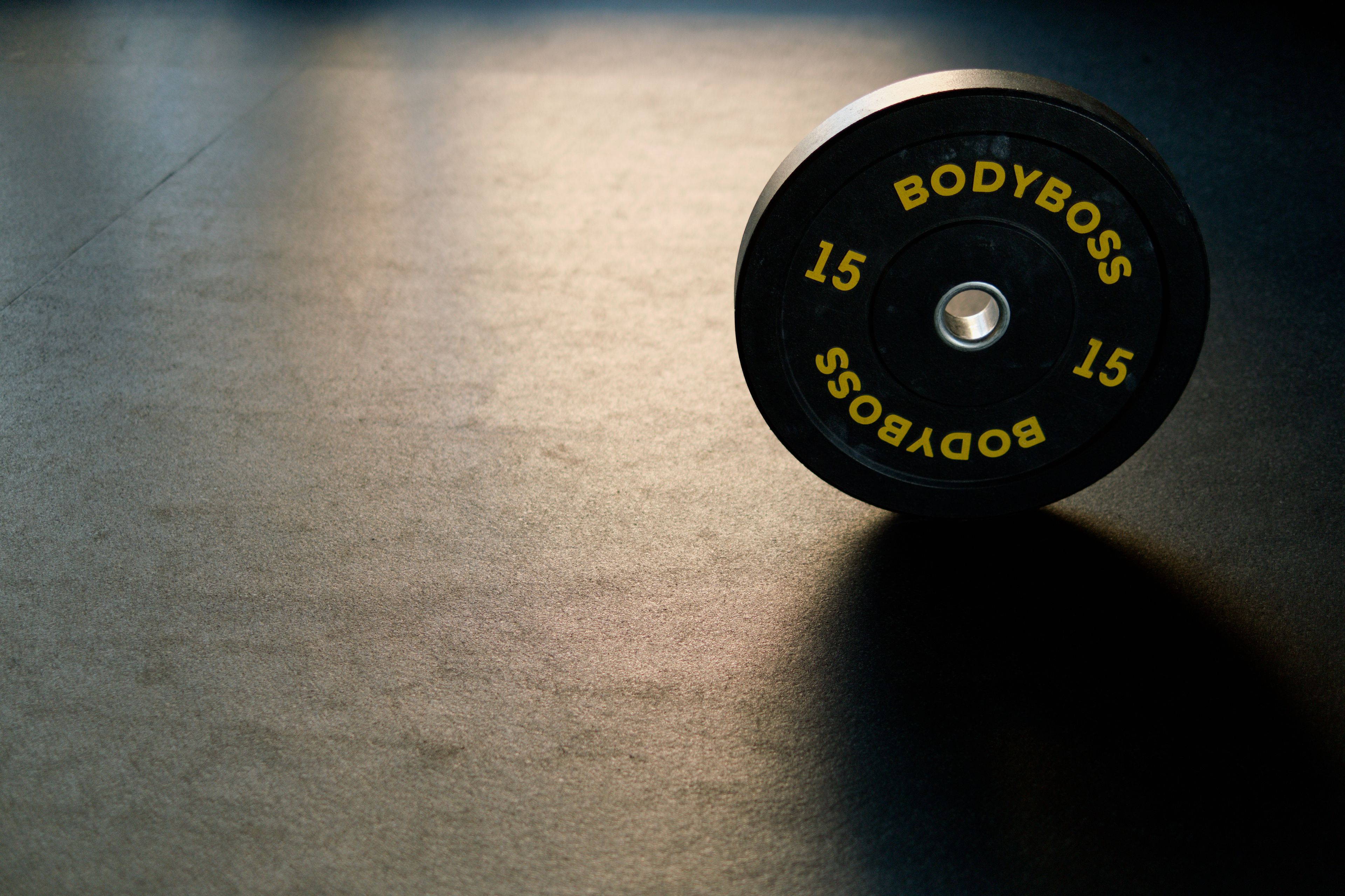 Black BodyBoss weight plate on gym floor, ideal for fitness and workout themes.