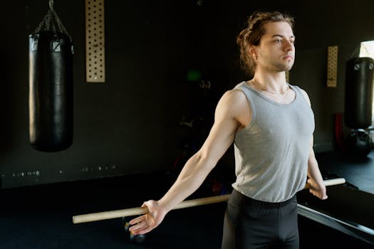 A man in a gym stretching with a rod next to a punching bag, emphasizing fitness and concentration.