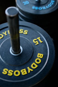 Detailed view of black barbell with 15 kg Boddyboss weight plates stacked.