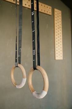 Close-up view of wooden gymnastic rings suspended in a fitness gym setting.