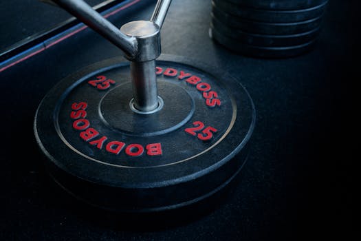 Close-up shot of a barbell with Bodyboss 25-pound weight plate in a gym.