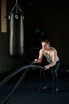 Focused man performing battle rope exercise in a fitness gym.