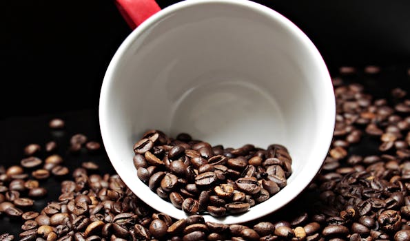 Close-up of roasted coffee beans spilling from a white mug on a dark surface, emphasizing the aroma and texture.
