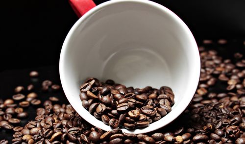 Free Close-up of roasted coffee beans spilling from a white mug on a dark surface, emphasizing the aroma and texture. Stock Photo