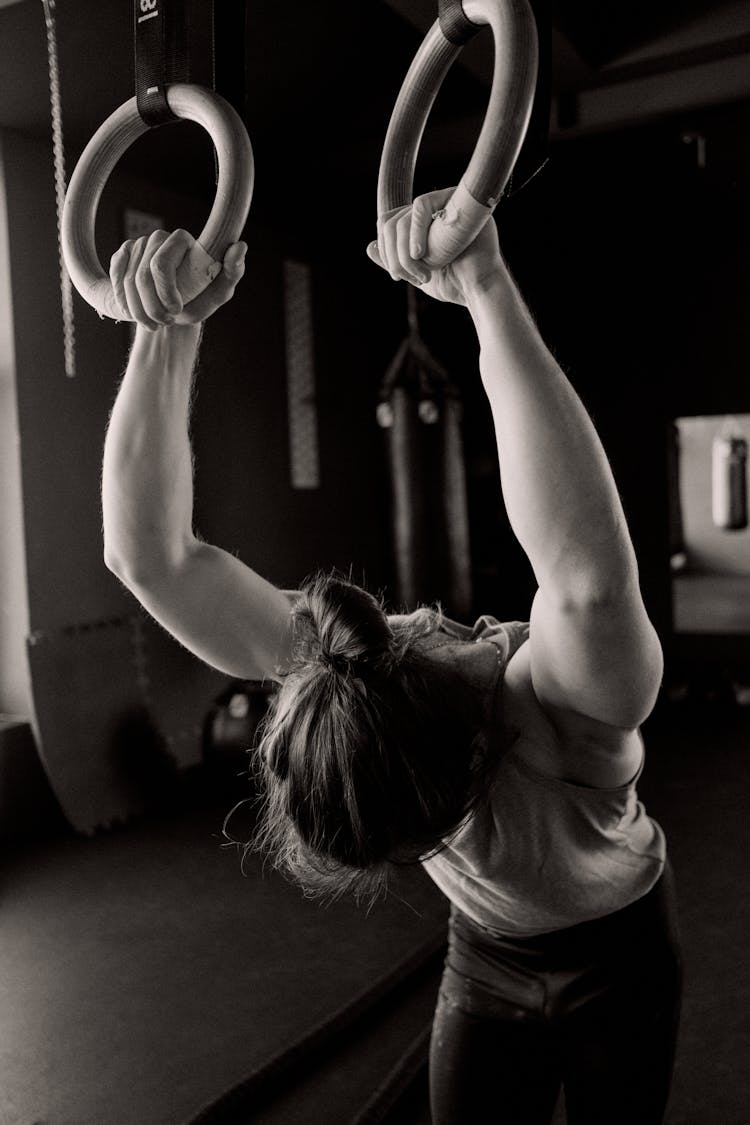 Grayscale Photo Of A Person Holding Gymnastic Rings