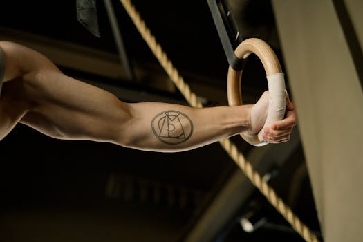Detailed view of an athlete's tattooed arm gripping a gymnastic ring in the gym.