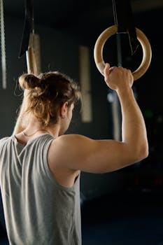 A male athlete working out on gymnastic rings in an indoor gym setting.
