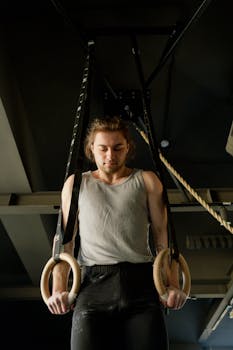 Focused man exercising on gymnastic rings at an indoor gym, showcasing strength and determination.