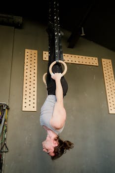 A man showcasing strength and skill while training upside down on gymnastic rings in a fitness gym.
