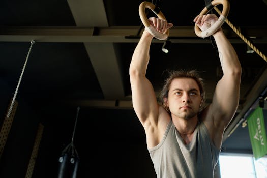 Focused young man exercising on gymnastic rings in a modern gym setting.