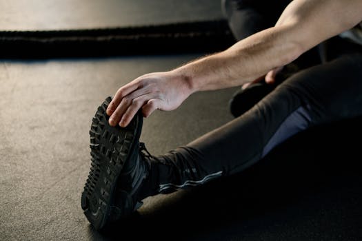 Close-up of a man's hand reaching for his foot while stretching on a gym floor.