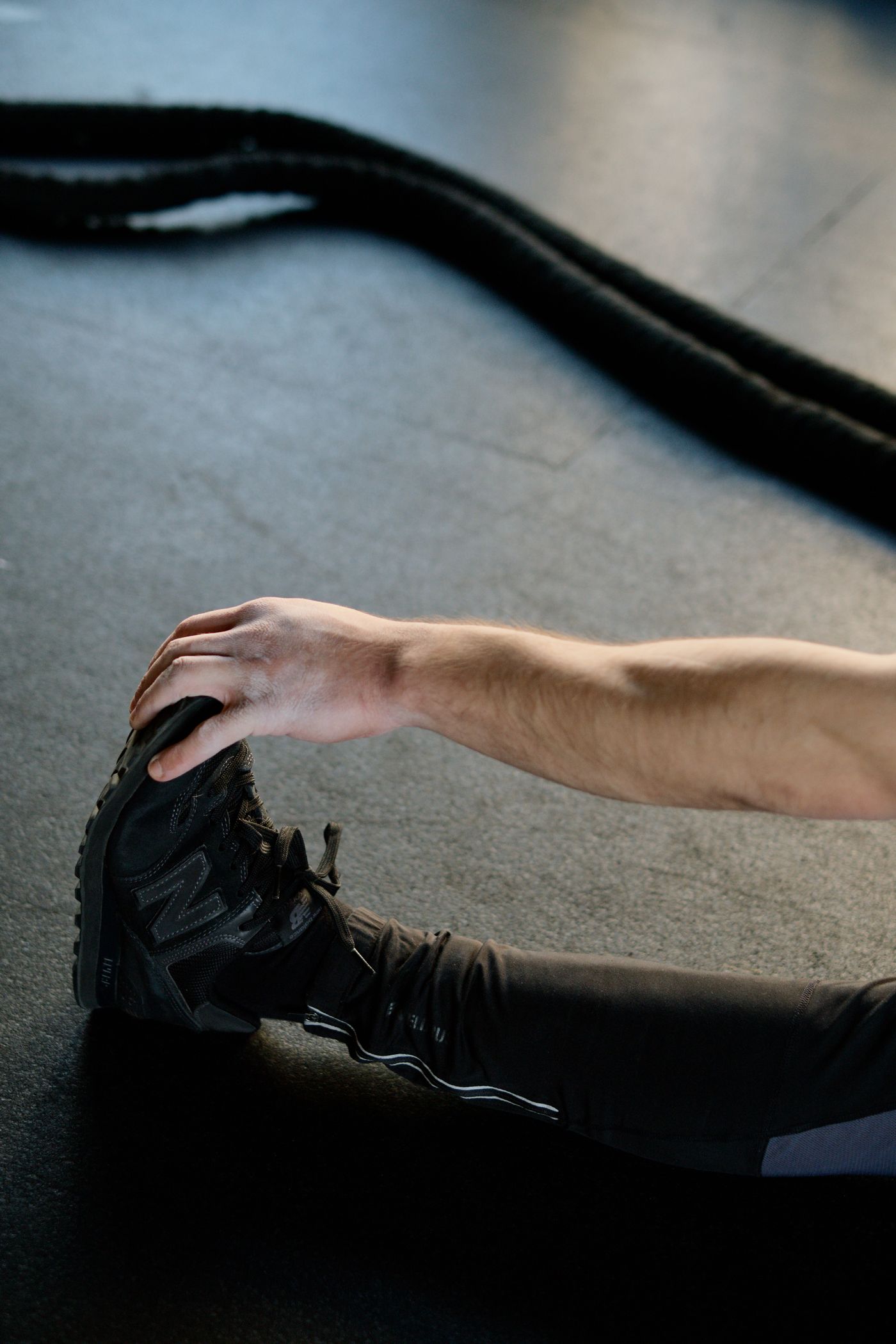 Athlete stretching on a gym floor with battle ropes and training equipment nearby