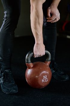 Close-up of a man's hand lifting a 32 kg kettlebell, showcasing strength in a gym environment.