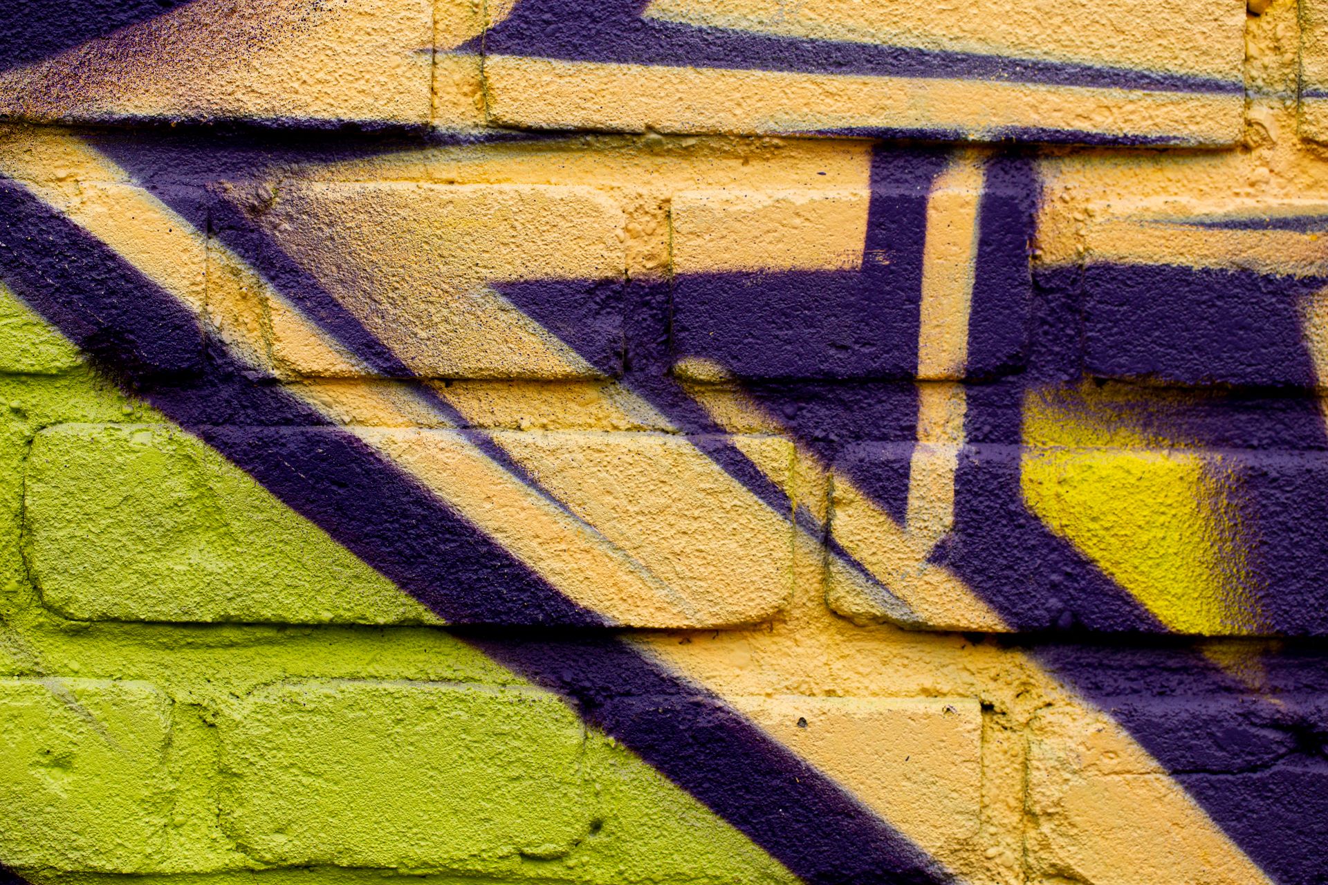 Purple, yellow and green spray-painted shapes on a brick wall