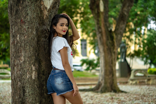 Back view of slim teenager with red lips wearing casual outfit standing in park