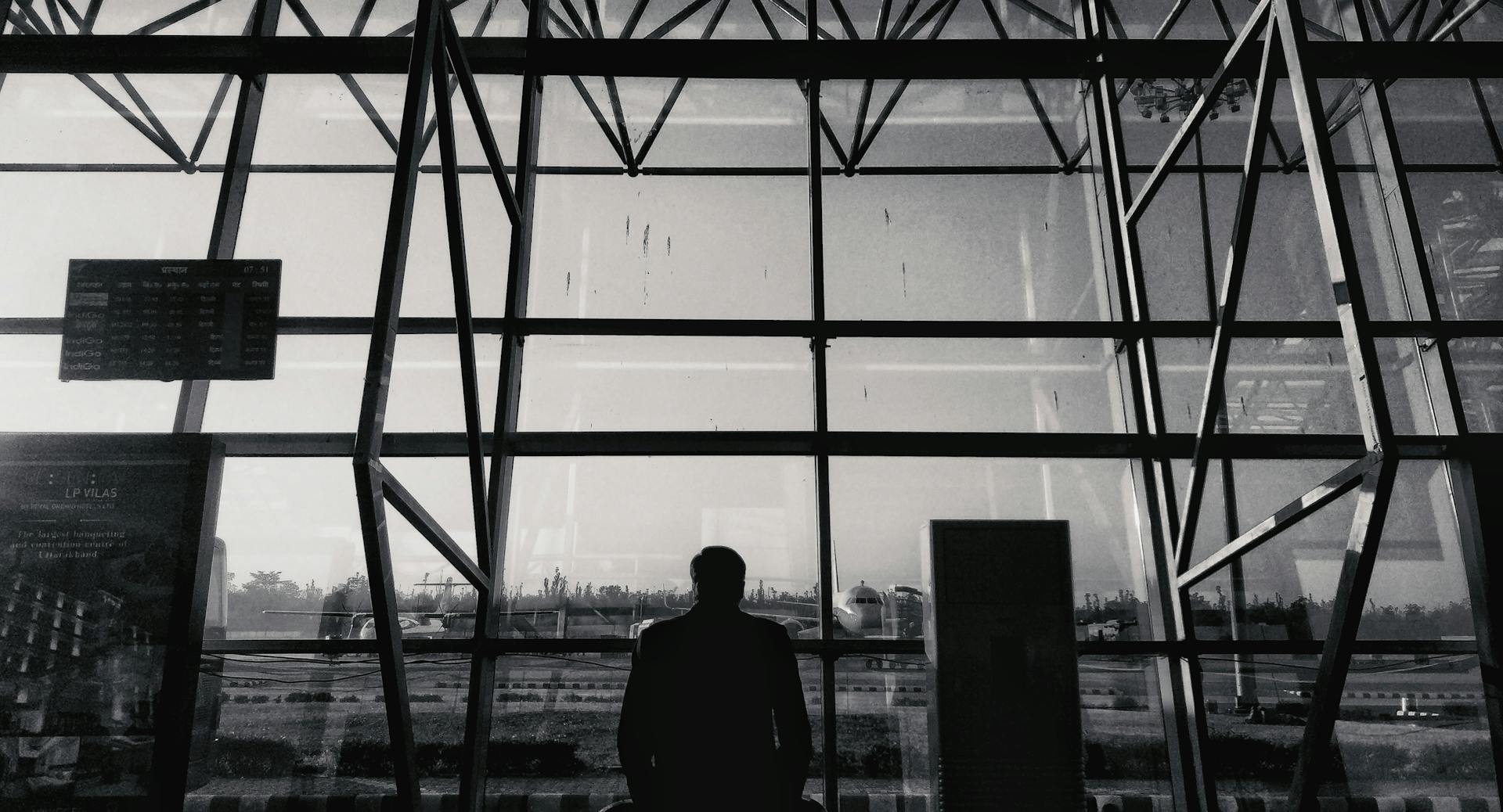 Silhouette of a man looking through glass windows at an airport terminal in Dehradun.