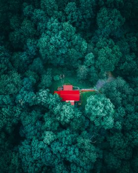 Drone view of small house with red rooftop located among green trees in woodland