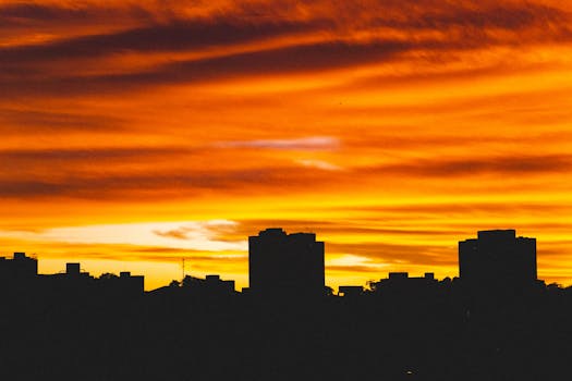 Picturesque low angle view of colorful sky with clouds illuminating silhouettes of buildings at sunset in dusk