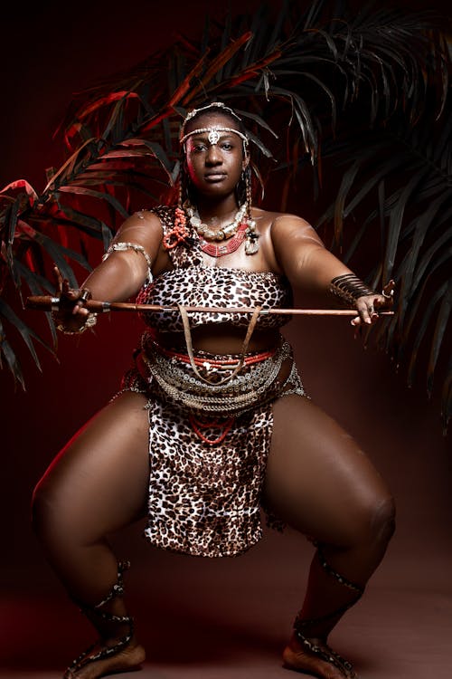 Black female dancer squatting with wooden stick at night