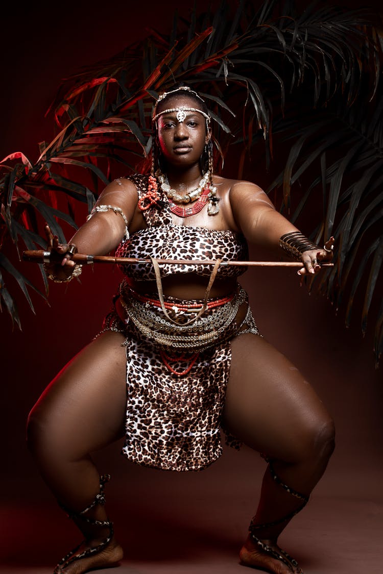 Black Female Dancer Squatting With Wooden Stick At Night