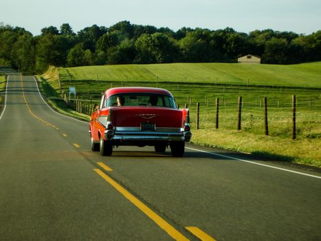 Classic red car driving on a scenic countryside road in Ohio, capturing a vintage travel vibe.